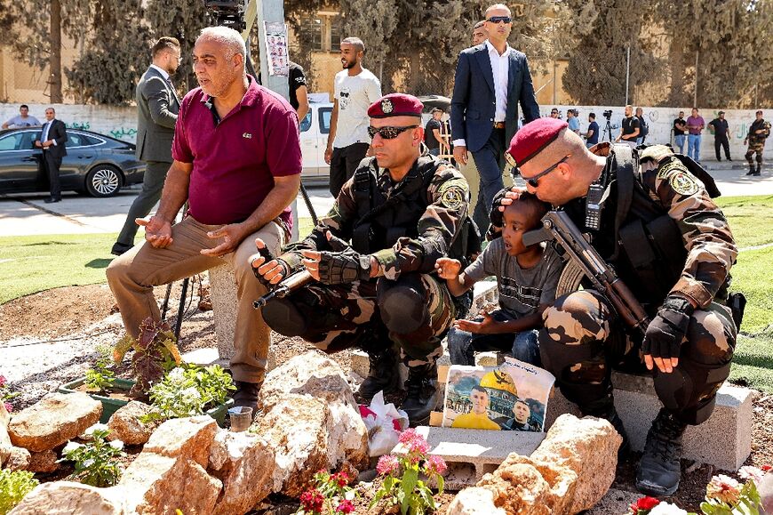 A Palestinian presidential guardsman kisses the head of a boy as they sit by the graves of Palestinians killed in the recent Israeli raid on Jenin camp