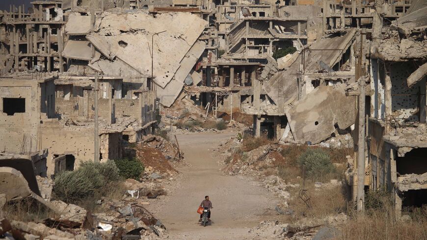 A picture taken on Aug. 2, 2018, shows a man riding a motorcycle past destroyed buildings in the opposition-held southern city of Daraa.