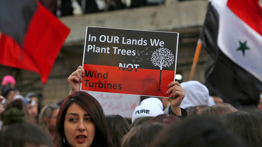 A woman holds up a sign as other protesters wave Syrian national flags and red banners during a demonstration by Druze residents of the village of Majdal Shams in the Israeli-annexed Golan Heights against Israeli construction of wind turbines in the territory, Jan. 24, 2020.