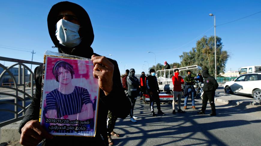 A man carries a picture of a demonstrator who was killed during ongoing anti-government protests, as other demonstrators block the street in Najaf, Iraq December 23, 2019. REUTERS/Alaa al-Marjani - RC2W0E9FX81T